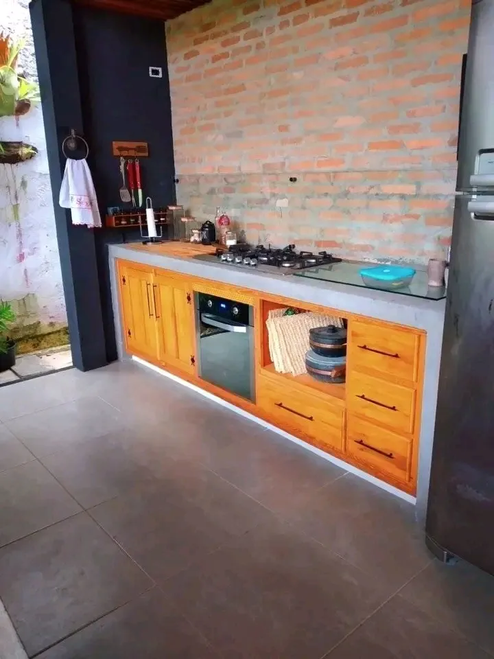 Cozinha de madeira maciça com cooktop, forno embutido e parede de tijolo aparente